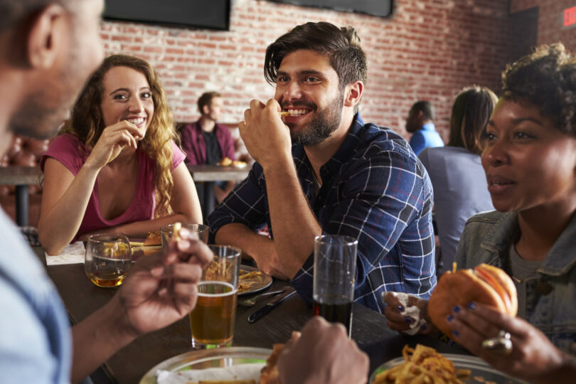 Friends Eating Out In Sports Bar With Screens In Background