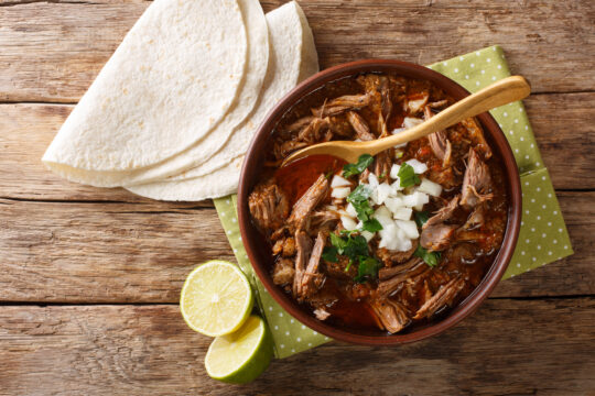 Guiso de res cocido a fuego lento al estilo mexicano Birria de Res servido con lima y tortilla en un tazón. Vista superior horizontal